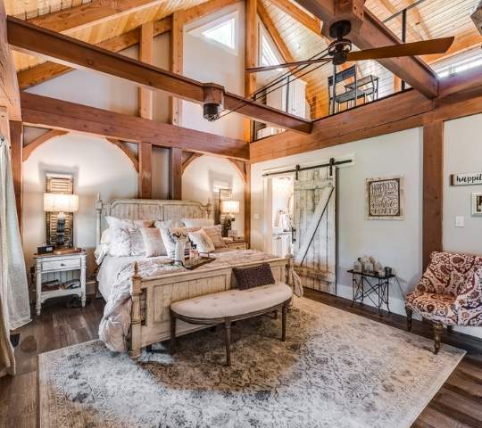 photo of master bedroom of log home with exposed a-frame beams and wood ceiling