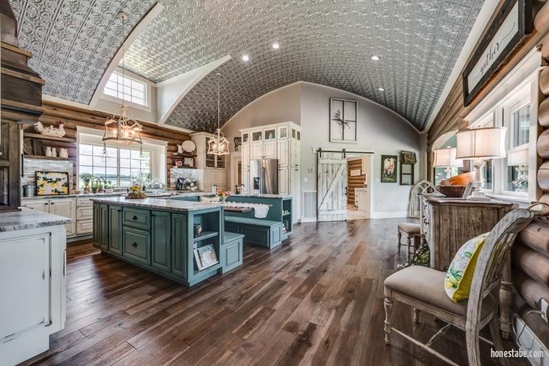photo of master kitchen with open plan, rounded tiled ceiling, central double island framing a bench dining area, white cabinets and built in appliances, including a cabinet framed refrigerator